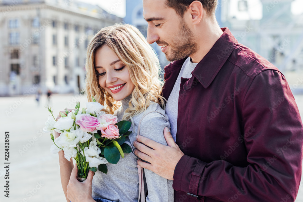 handsome boyfriend hugging attractive girlfriend with bouquet in city handsome boyfriend hugging attractive girlfriend with bouquet in city