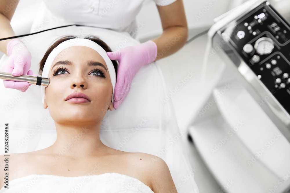 A woman came to laser hair removal facial. The woman lies and smiles, the doctor leads him in the face with a modern laser epilator. They are in the modern clinic.close up A woman came to laser hair removal facial. The woman lies and smiles, the doctor leads him in the face with a modern laser epilator. They are in the modern clinic.close up