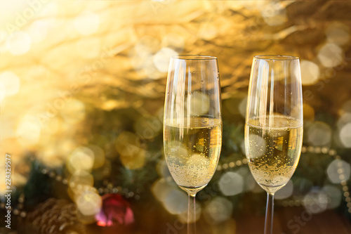 two New Year's glasses with champagne wine on a wooden table and a gold a white background in the glare with a blur