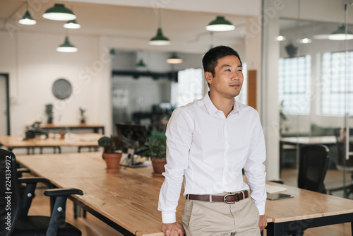 Photography Young Asian businessman standing in an office deep in thought