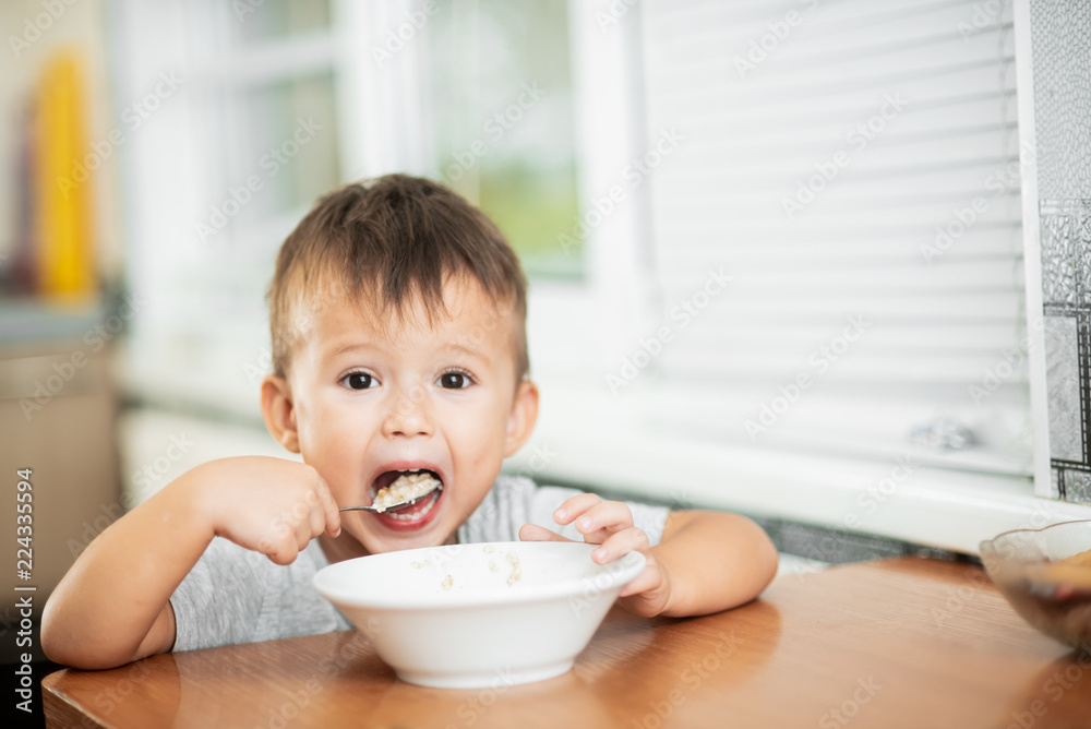 charming child in the kitchen eating oatmeal charming child in the kitchen eating oatmeal