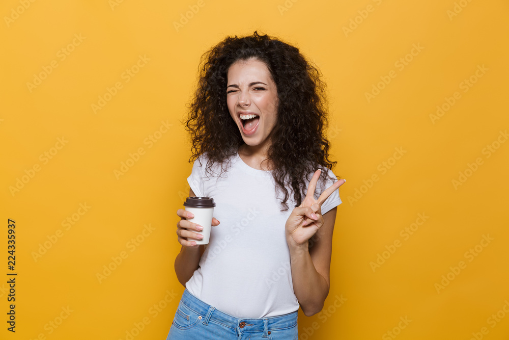 Image of young european woman 20s with curly hair smiling and holding takeaway coffee in paper cup, isolated over yellow background Image of young european woman 20s with curly hair smiling and holding takeaway coffee in paper cup, isolated over yellow background