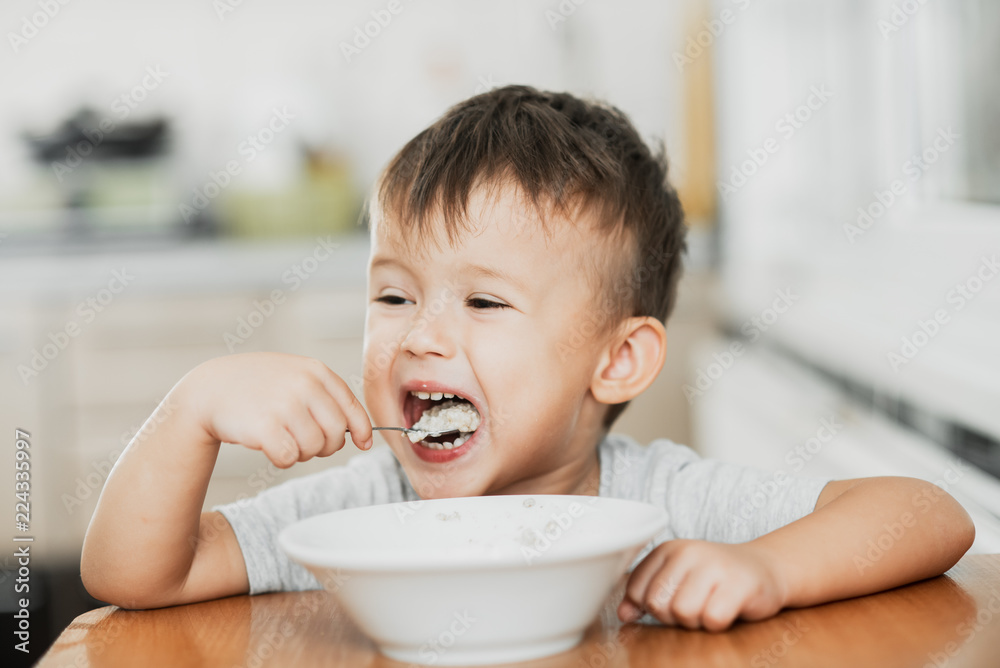 charming child in the kitchen eating oatmeal charming child in the kitchen eating oatmeal