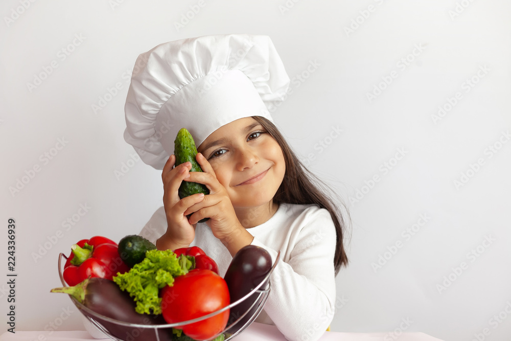 Cute girl in chef uniform eating cucumber on light background. 