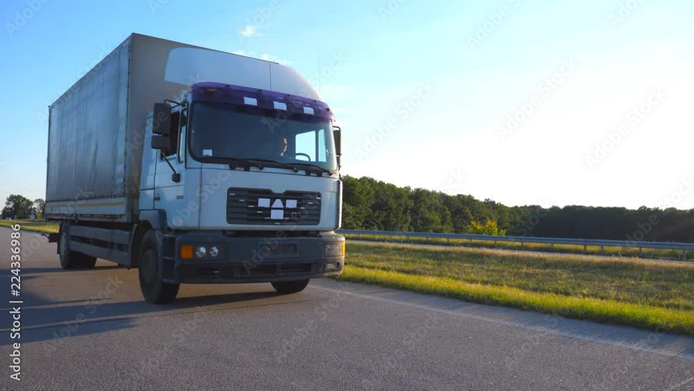 Camera follows to truck driving on a highway. Lorry rides through the countryside with beautiful landscape at background. Front view Slow motion Close up