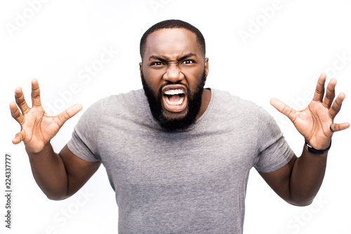 Portrait of dark-skinned African guy screaming with wide opened mouth in despair having unhappy, crazy, agressive, angry, dangerous expression. Frustrated male shouting loudly having aggression