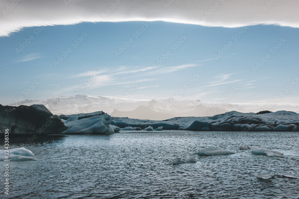 glacier ice pieces floating in lake in Jokulsarlon, Iceland under blue sky with mountains on background