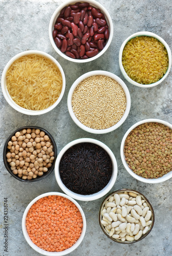 Variation of cereals in bowls: beans, rice, chickpeas, peas on a concrete background.