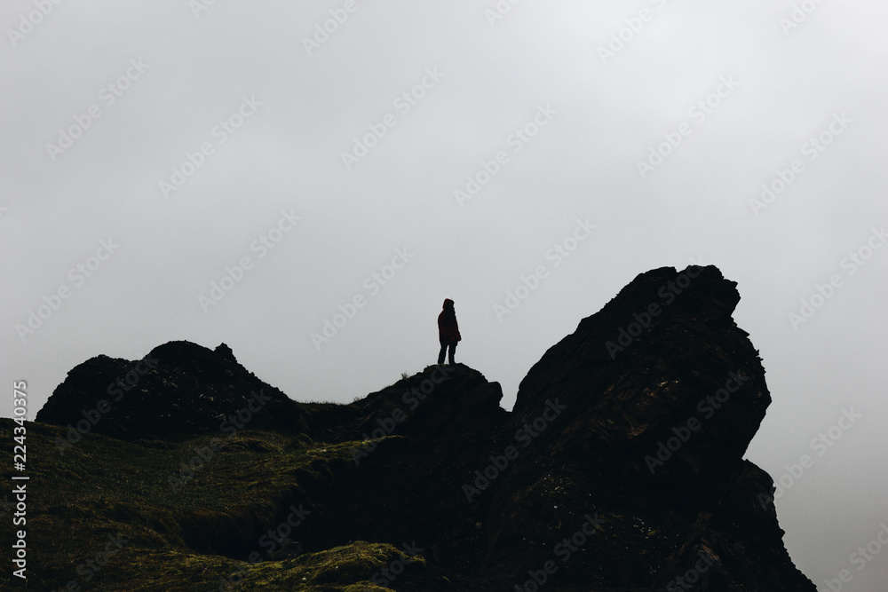 Silhouette of woman standing on rock in front of cloudy sky