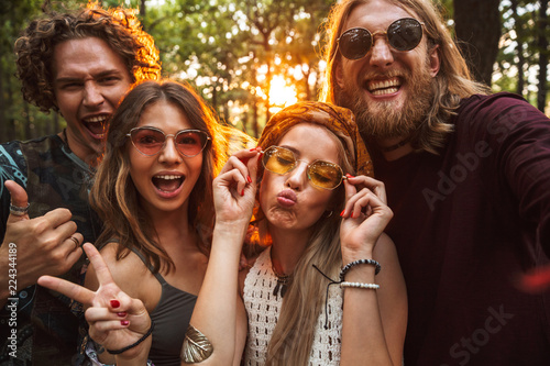 Photo of friendly hippie people men and women, smiling and taking selfie in forest