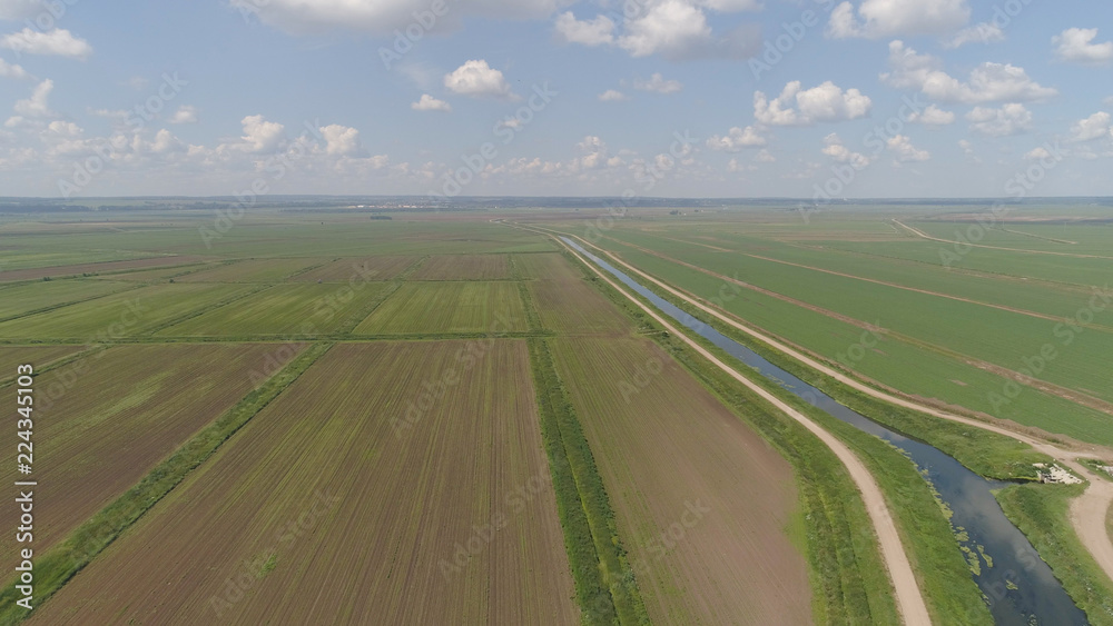 Aerial view of agricultural cultivated fields with irrigational channel. Agricultural landscape rows. Irrigated farmland. Countryside with fields of crops.