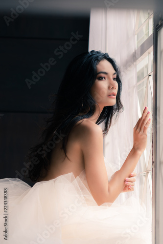 Portrait of sexy young woman in white dress posing near windows