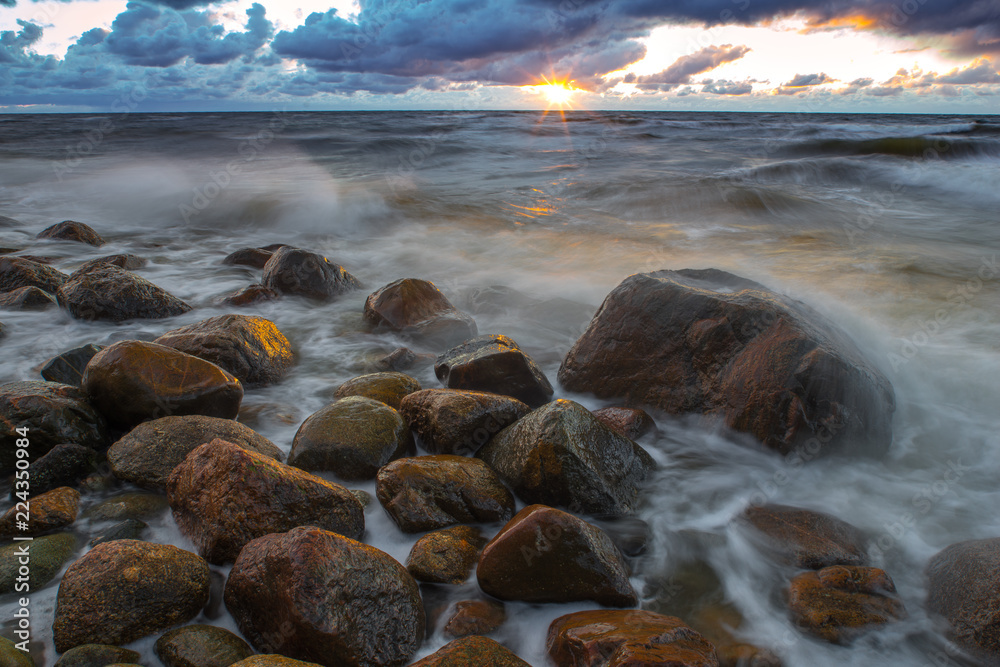 Obraz premium A sea landscape with rocks, a storm and a setting sun. Waves, rocks, storm and clouds. 