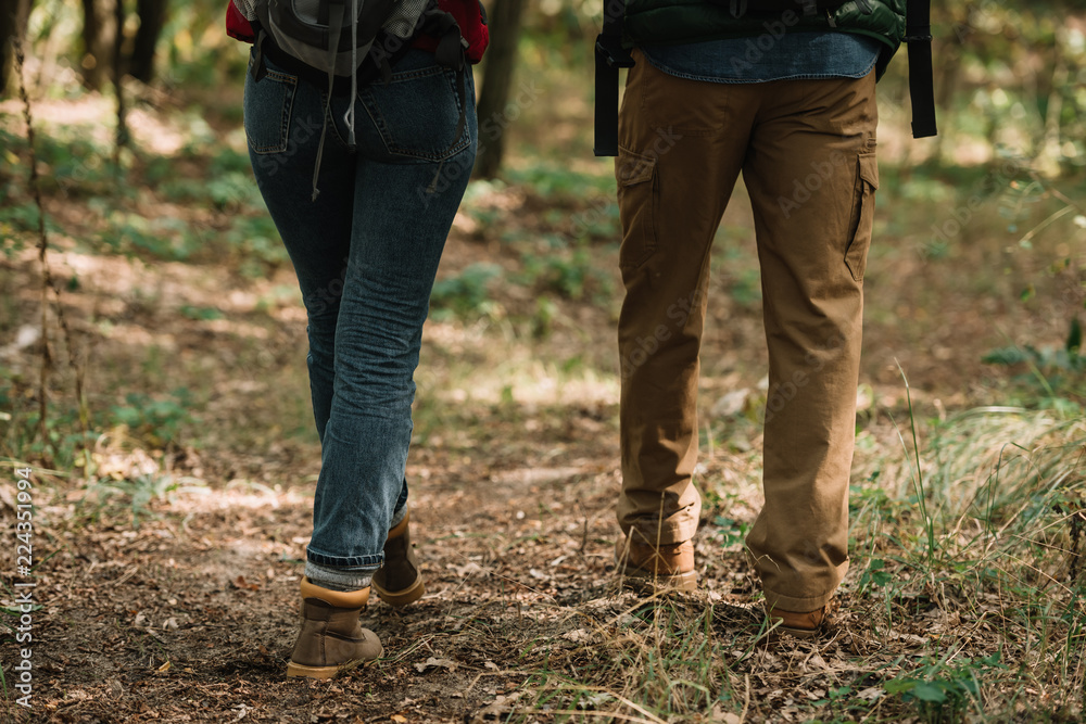 partial view of couple of travelers hiking in forest