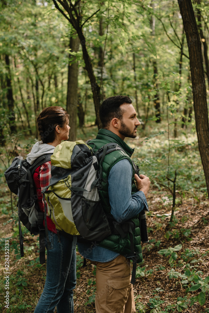 side view of man and woman with backpacks hiking in woods together