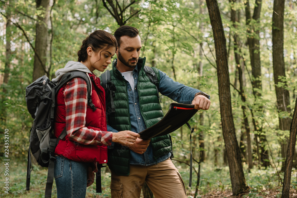 man and woman looking for destination on map while hiking in forest together man and woman looking for destination on map while hiking in forest together