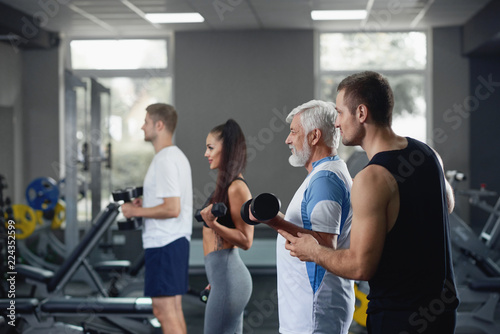 Elderly man doing exercise with group of younger people at gym.