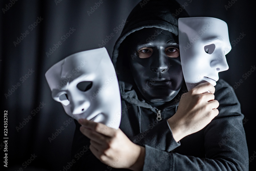 Mystery hoody man wearing black mask holding two white masks in his hand.  Anonymous social masking. Major depressive disorder or bipolar disorder.  Halloween concept Stock Photo | Adobe Stock