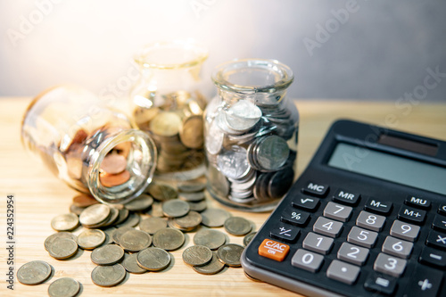 Calculator with coin in currency glass jar and spilling on wooden table. Compound interest rate calculation. Financial business plan. Saving money for future retirement concept