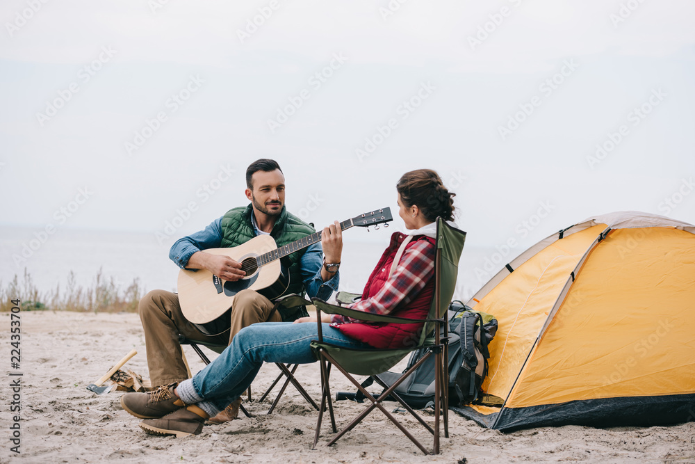 man playing acoustic guitar for wife on camping