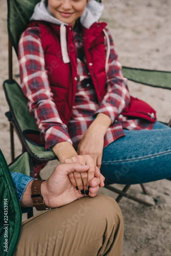 partial view of man and woman holding hands while enjoying camping together