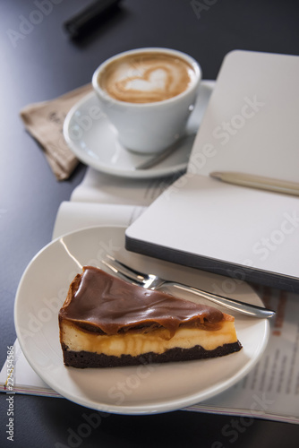 Caramel cheesecake with cappuccino and magazines. Morning meal. 
