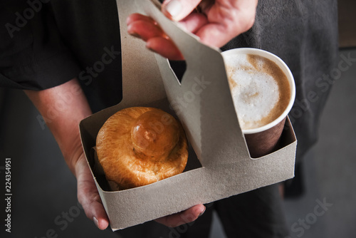 Woman is holding a take away card-box basket with coffee and cake. Food and drink conception.