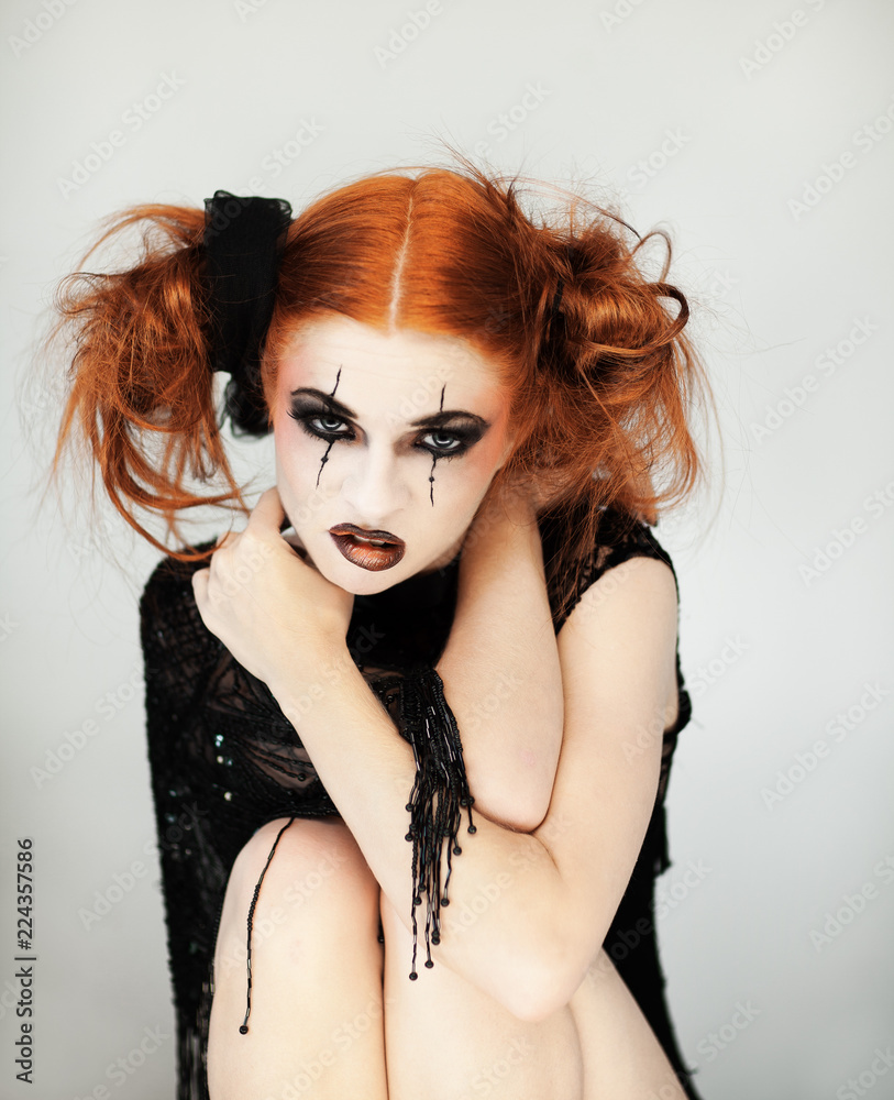 Obraz premium Beautiful, cute woman with halloween make up and red hair poses in front of white background