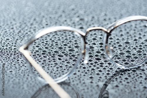 close up view of eyeglasses and water drops on grey backdrop