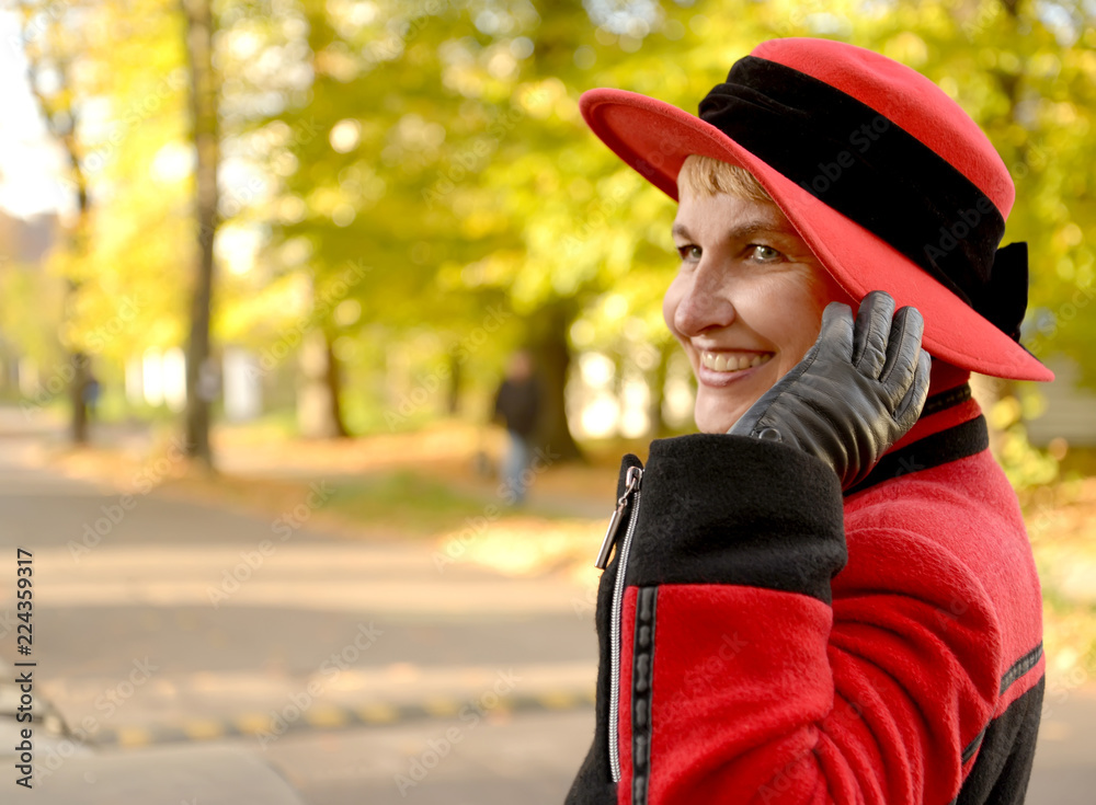 The joyful woman holds a hat with a hand on the autumn street