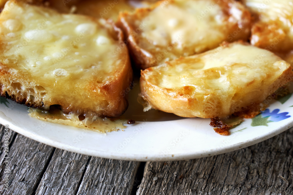 Toasts with melted cheese in an old plate on wooden boards Toasts with melted cheese in an old plate on wooden boards