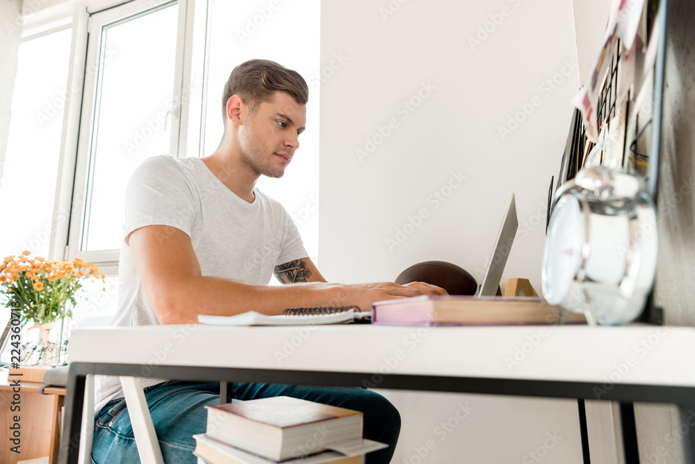 side view of focused man using laptop at table at home office side view of focused man using laptop at table at home office