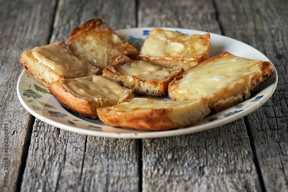 Toasts with melted cheese in an old plate on wooden boards Toasts with melted cheese in an old plate on wooden boards