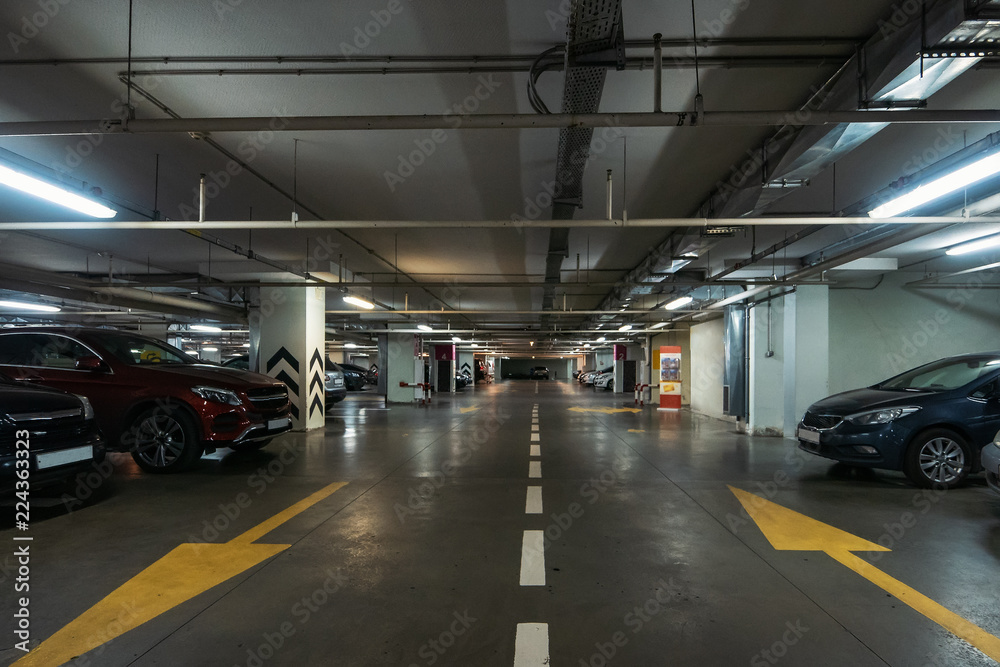 Illuminated underground car parking interior under modern mall with lots of vehicles and arrows on floor Illuminated underground car parking interior under modern mall with lots of vehicles and arrows on floor