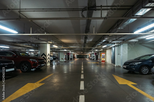 Illuminated underground car parking interior under modern mall with lots of vehicles and arrows on floor © DedMityay