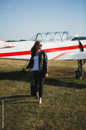 Girl with a blue bag near the small aircraft. Concept of woman who returned from travel on private airplane.