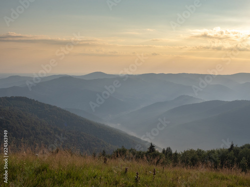 Evening sky above the dark mountain ranges. Carpathians mountains at summer, west Ukraine. Nature background. Dark peaks covered with evening fog. Hillsides with dense forest. Blurred background