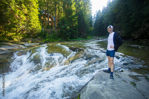 Young man walk near fast river in middle of forest