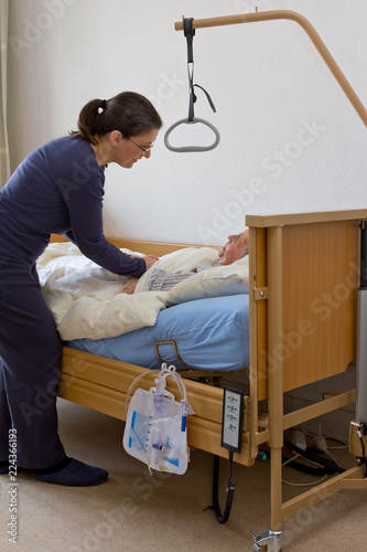 Woman at the nursing bed of her terminally ill grandmother, holding her hand, talking to her and keeping company. Concept of dying at home or in a hospice. photo