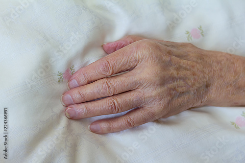 One gaunt hand of an old woman with a terminal illness like cancer on a light duvet cover, concept of death, dying