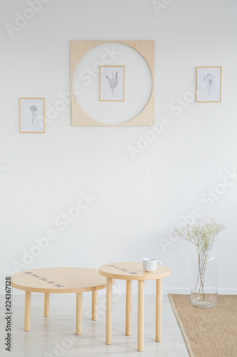 Wooden tables and flowers in white minimal living room interior with posters and rug. Real photo
