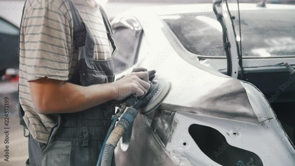 Man mechanic grinds the painted car body with a grinder Man mechanic grinds the painted car body with a grinder