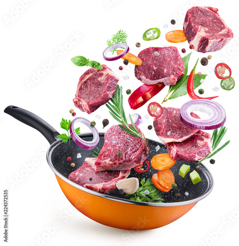 Flying meat steaks and spices over a frying pan. File contains clipping path.