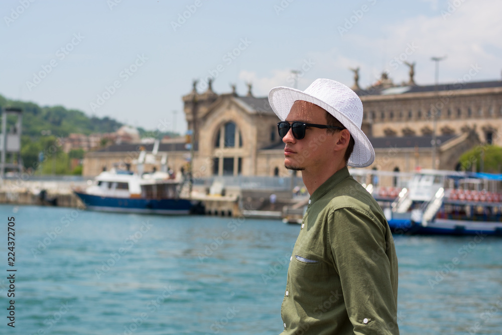 A young guy in a hat, sunglasses stands in the port of Barcelona's at the port customs background, Barcelona, Spain