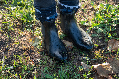 Black wet gumboots on the ground with grass and yellow leaves