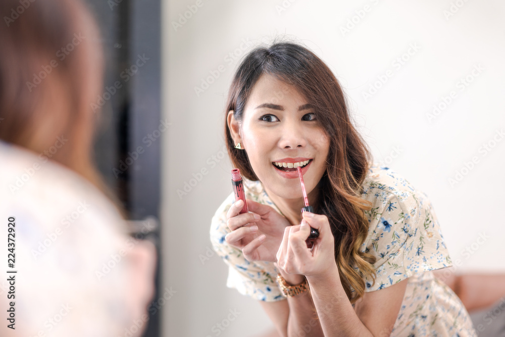 Beautiful young asian woman professional beauty blogger applying makeup, charming girl look at mirror, use lip brush for lipstick dyes her lips lipstick pink. doing a make up tutorial. Selective focus Beautiful young asian woman professional beauty blogger applying makeup, charming girl look at mirror, use lip brush for lipstick dyes her lips lipstick pink. doing a make up tutorial. Selective focus