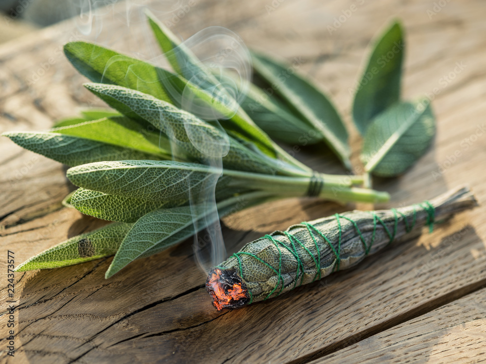 Burning sage stick and fresh sage leaves on the wooden background.  Stock-Foto | Adobe Stock