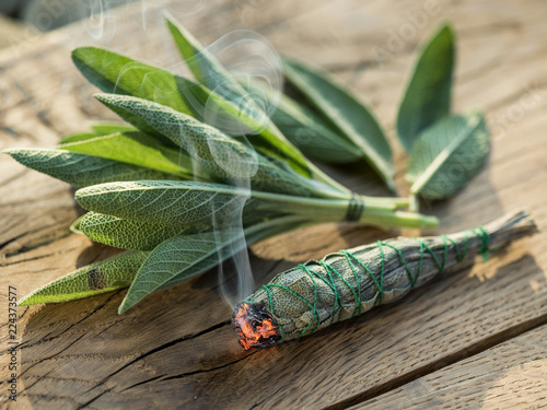 Burning sage stick and fresh sage leaves on the wooden background. photo