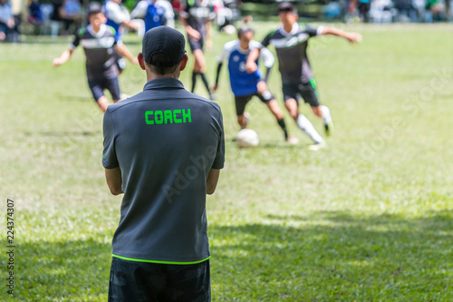Male soccer or football coach standing on the sideline watching his team play