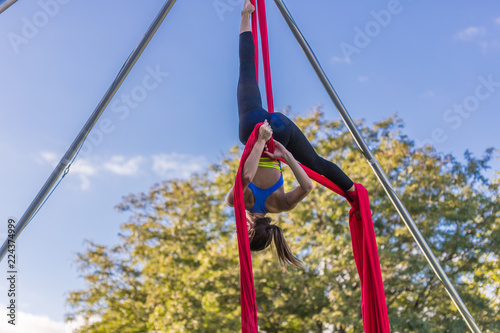 Woman in blue dance is hanging upside down on red ribbon
